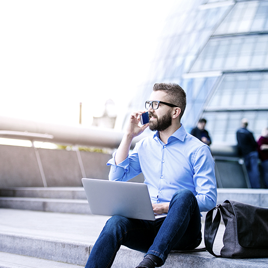 man sitting outside with a laptop on the phone