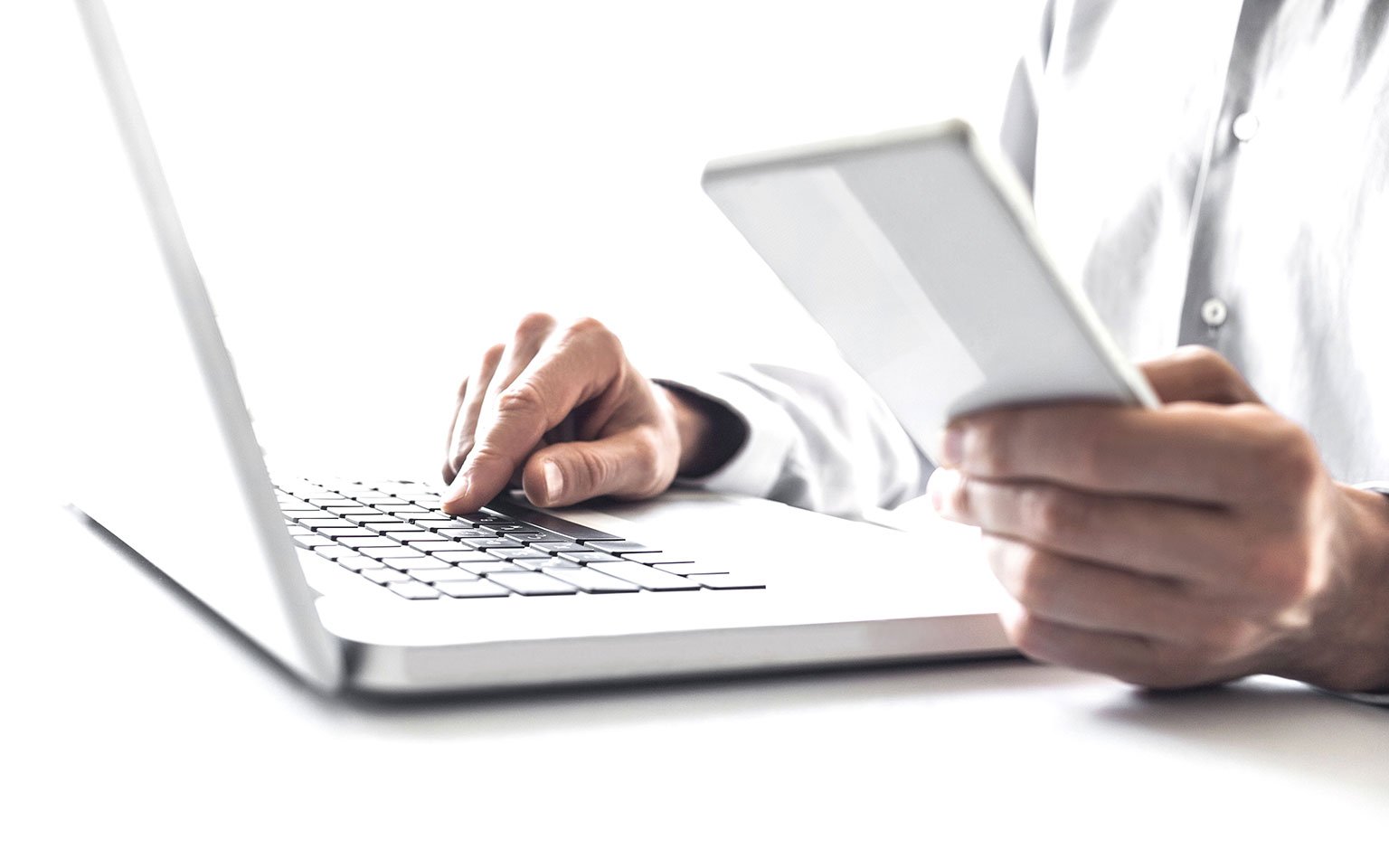 man typing on laptop and holding tablet